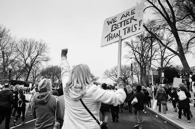 black and white image of a climate rally showing a woman from behind holding a sign that reads: 'we are better than this'.