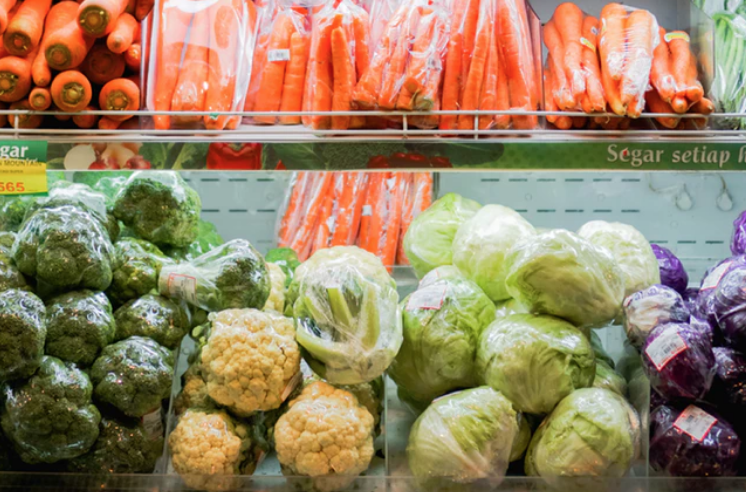 refrigerated shelf in supermarket with an array of vegetables including cauliflower, carrots, broccoli and cabbage.
