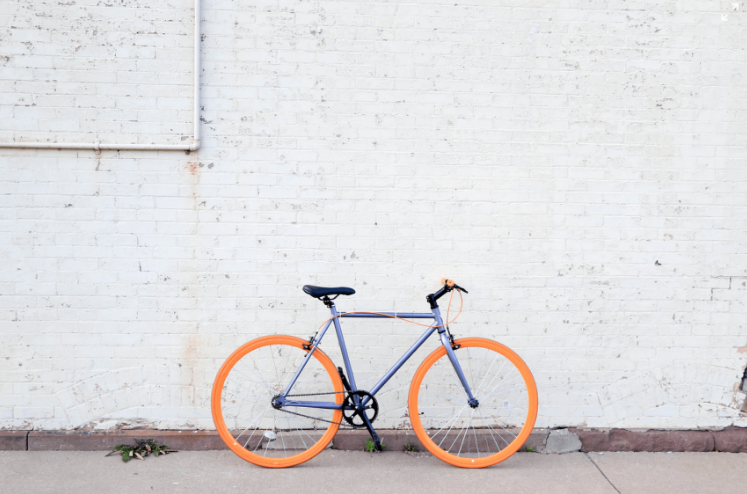 blue bike with orange wheels against a white wall