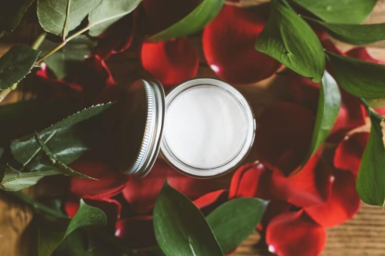 tub of organic skincare amongst rose petals and leaves.