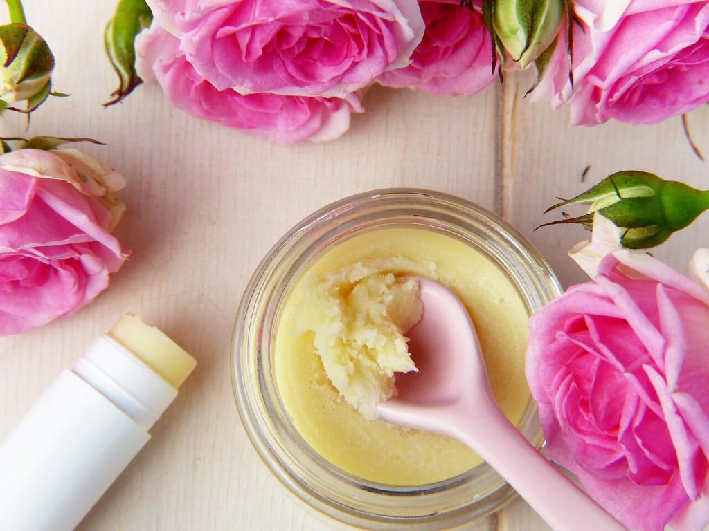 tub of shea butter with a plastic spoon in it amongst pink roses.