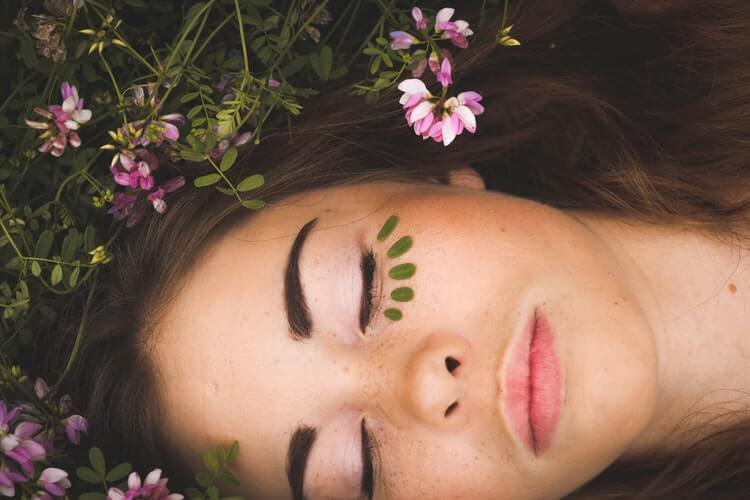 pretty girl lay on top of some shrubbery with her eyes closed and leaves under her eyes 