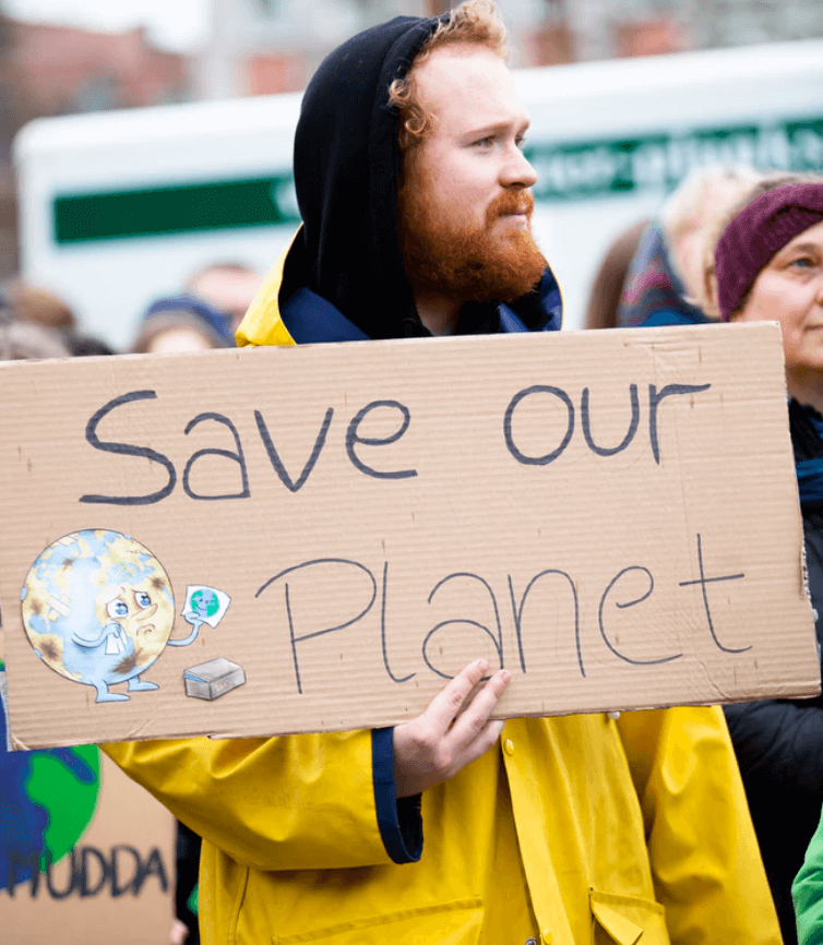 Ginger man in a yellow jacket holding a sign saying save our planet.