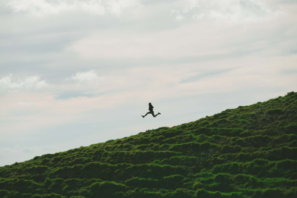 silhouette of person leaping down a grassy hill.