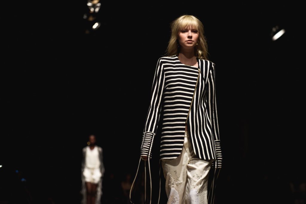 Fashion week showing a woman in a black and white striped jacket and white trousers.