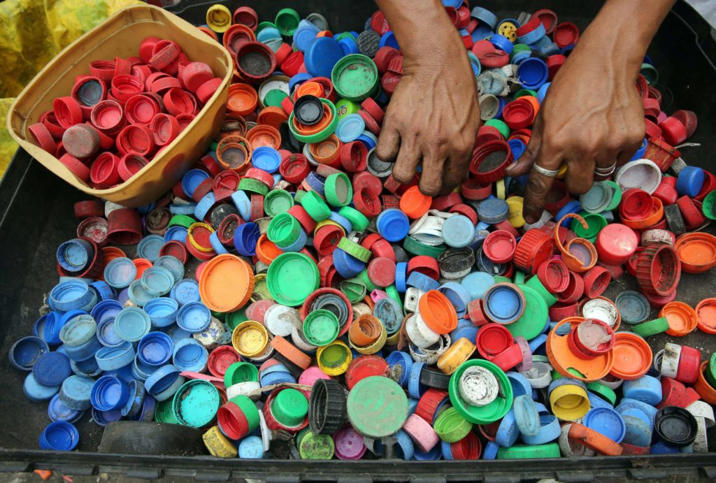 Hands sorting though hundreds of multi coloured bottle caps.