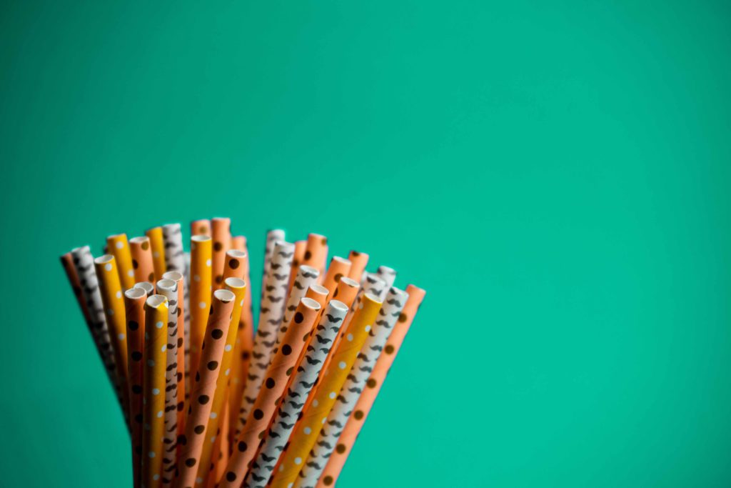 orange, yellow and white paper straws against a bright turquoise background