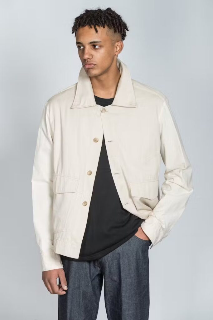 Model wearing cream jacket, black t shirt and dark grey trousers