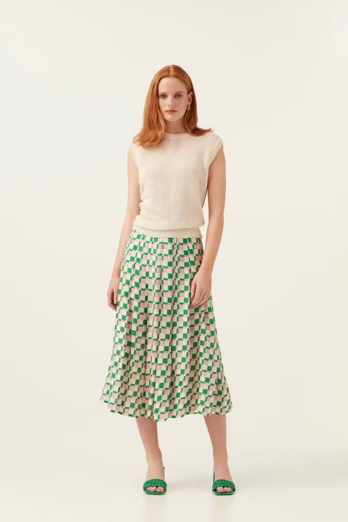 Model wearing beige vest top and green and white skirt and green shoes